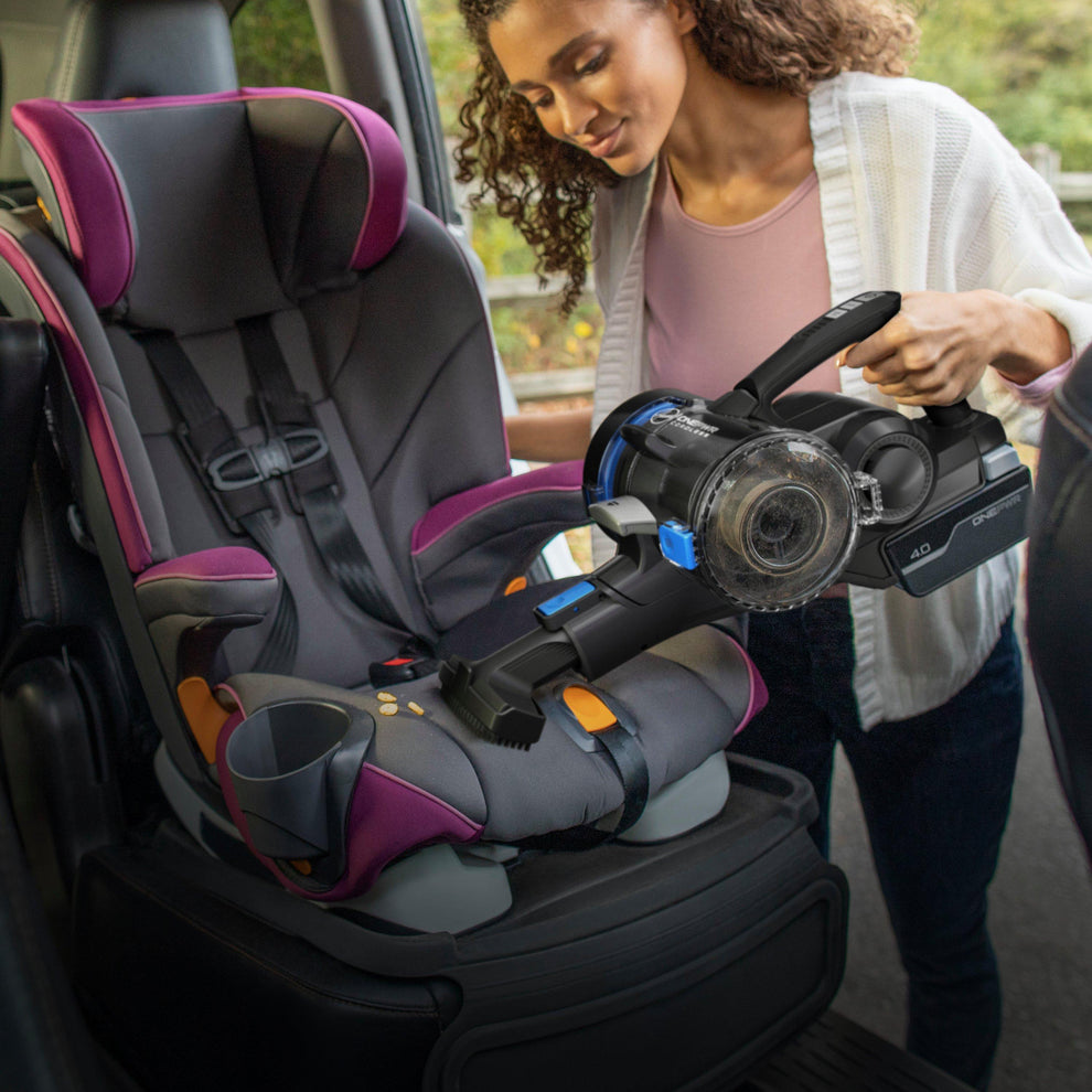 Person using a cordless handheld vacuum cleaner to clean a child's car seat, highlighting the vacuum's portability and effectiveness in reaching tight spaces for thorough cleaning.