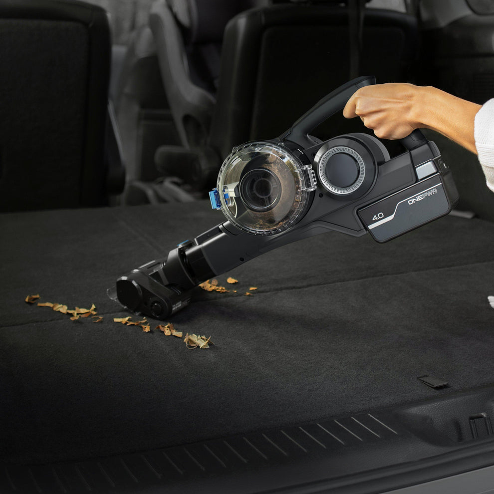 Handheld cordless vacuum cleaner being used to clean debris from the back of a car, showing its portability and efficiency in tight spaces.