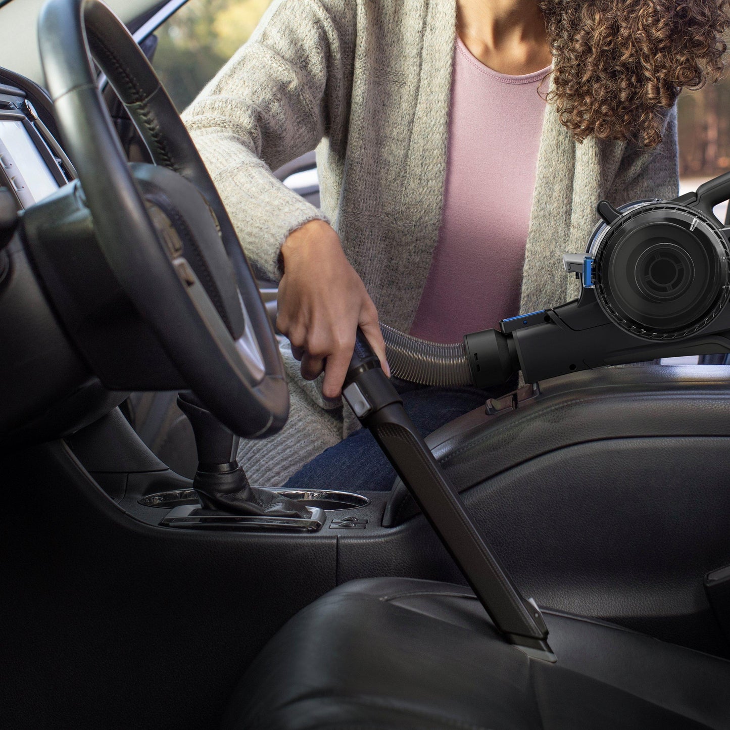 Person using a handheld cordless vacuum cleaner with a crevice tool attachment to clean tight spaces in a car's interior, demonstrating its versatility and effectiveness.