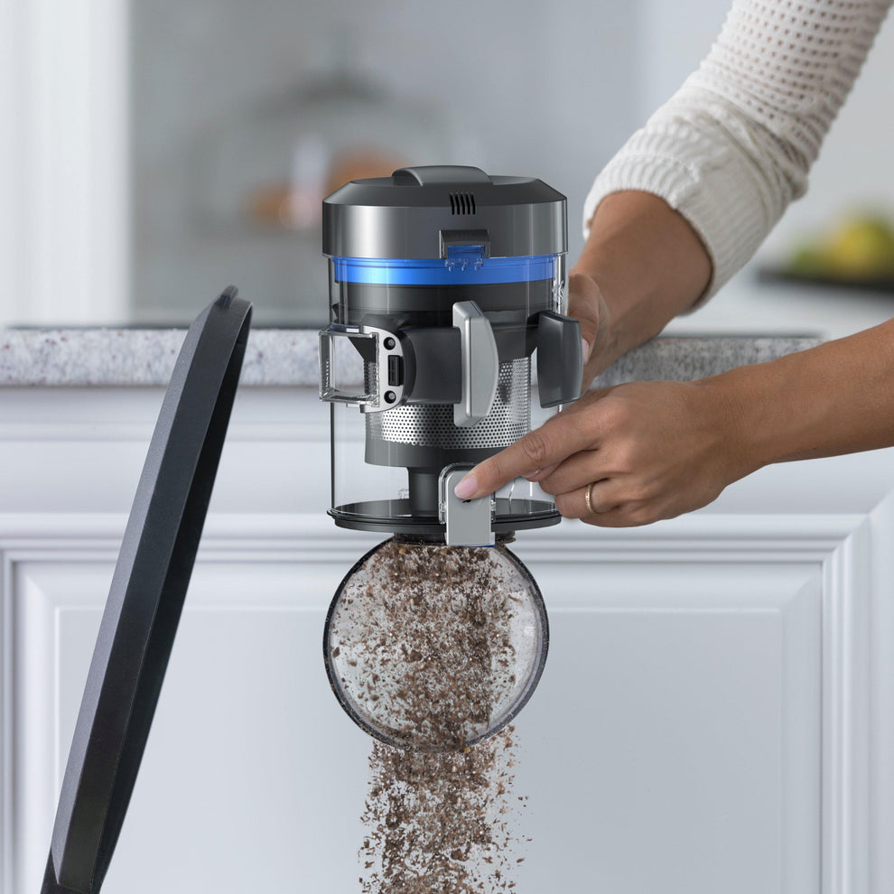Person emptying the dirt canister of a cordless vacuum cleaner into a trash bin, demonstrating the easy-to-use dirt release mechanism for quick and mess-free disposal.