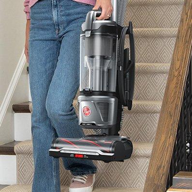 Person carrying a lightweight Hoover vacuum cleaner down a carpeted staircase, highlighting its portable and easy-to-handle design.