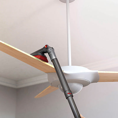 A vacuum cleaner extended length crevice tool attachment being used to clean a ceiling fan blade, demonstrating its capability to reach high and difficult areas for effective dust removal