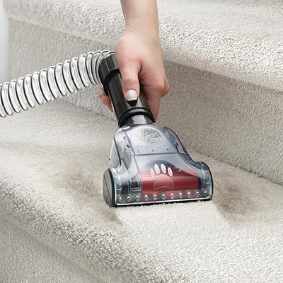 Close up of hand using the Hoover pet turbo tool, specifically designed for pet hair removal, to vacuum hair from a carpeted staircase.