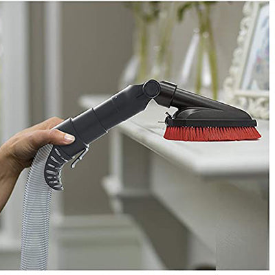 A hand using the Hoover dusting brush attachment to clean a white shelf, showcasing its ability to effectively remove dust and debris from delicate surfaces and furniture