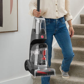Person carrying a lightweight Hoover carpet cleaner up the stairs for easy portability.