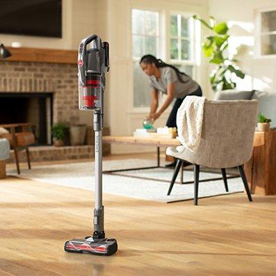 ONEPWR emerge cordless stick standing by itself as woman continues cleaning the living room showcasing its convenient design.