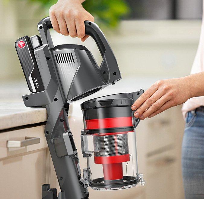 A person holding a Hoover vacuum cleaner while removing the dustbin for emptying.  The vacuum features a 4Ah ONEPWR battery, highlighting the ease of maintenance and convenience of the cordless design.