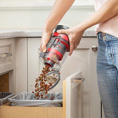 Person emptying their dustbin in the trashcan demonstrating the hassle free disposal of collected debris directly into the trash can, highlighting its convenient design for easy clean up.