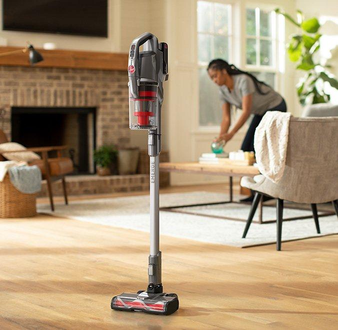 ONEPWR emerge cordless stick standing by itself as woman continues cleaning the living room showcasing its convenient design.