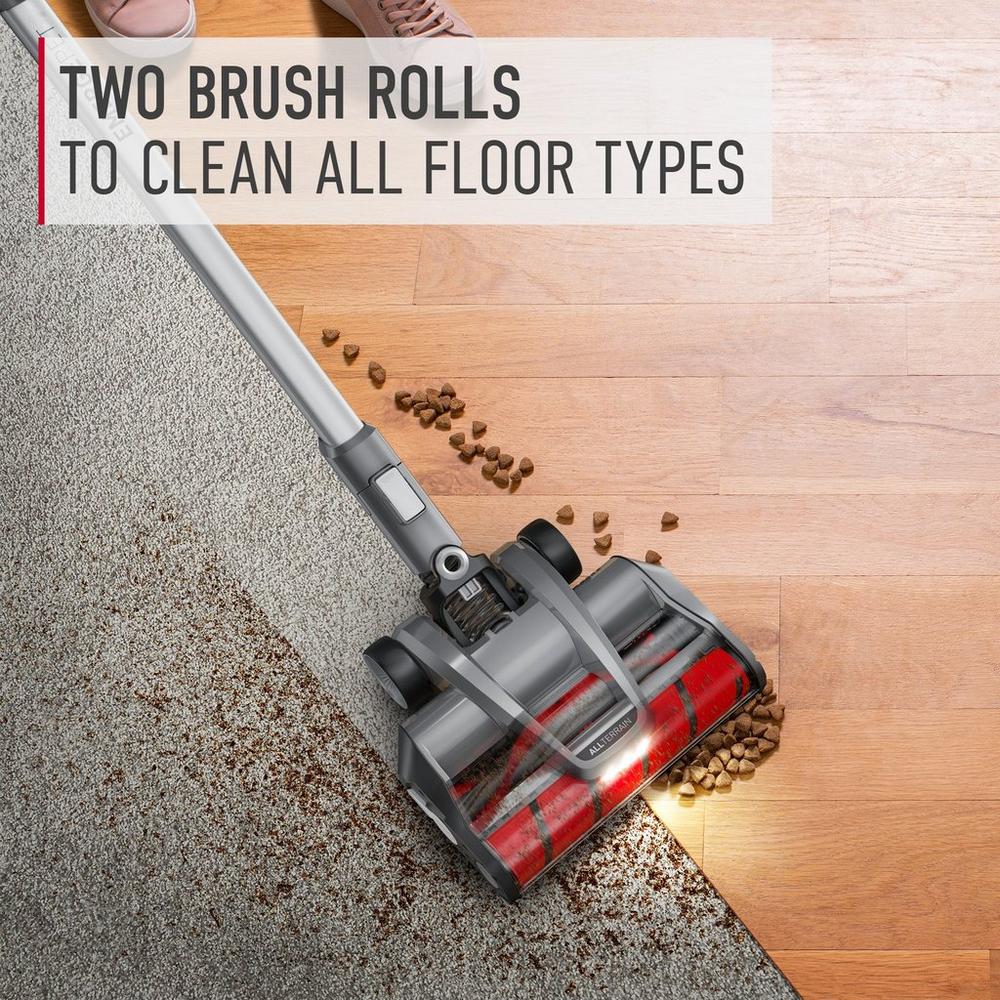 Hoover vacuum cleaner demonstrating its ability to clean both carpet and hard floor types with two brush rolls. The vacuum is shown picking up pet food from both surfaces, highlighting its versatility