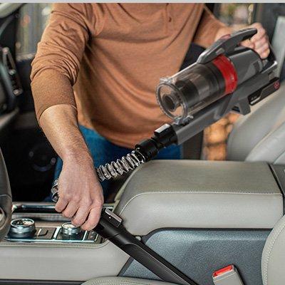 Person using their ONEPWR Emerge cordless vacuum cleaner with crevice tool to clean in between car seats, making it ideal for interior cleaning.
