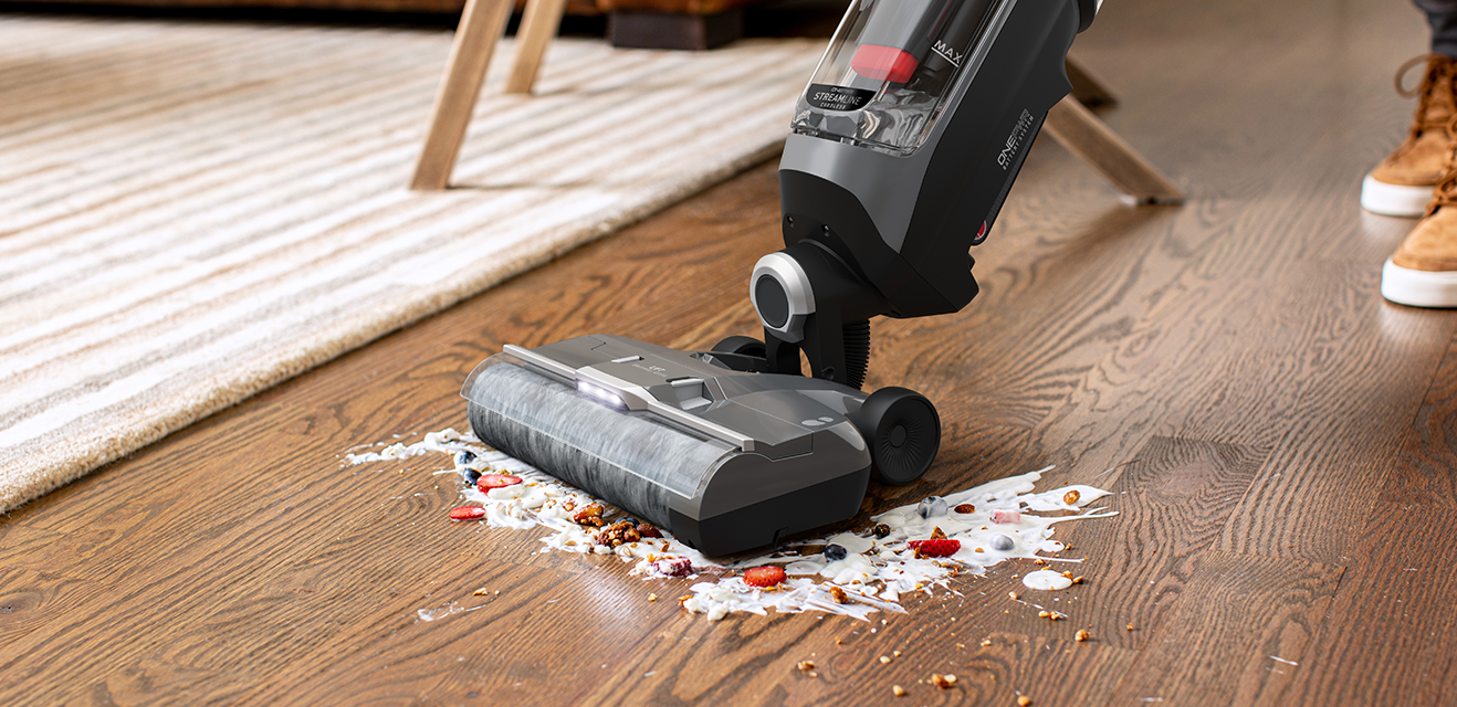 Vacuum cleaner cleansing a wooden floor that has a food spill on it