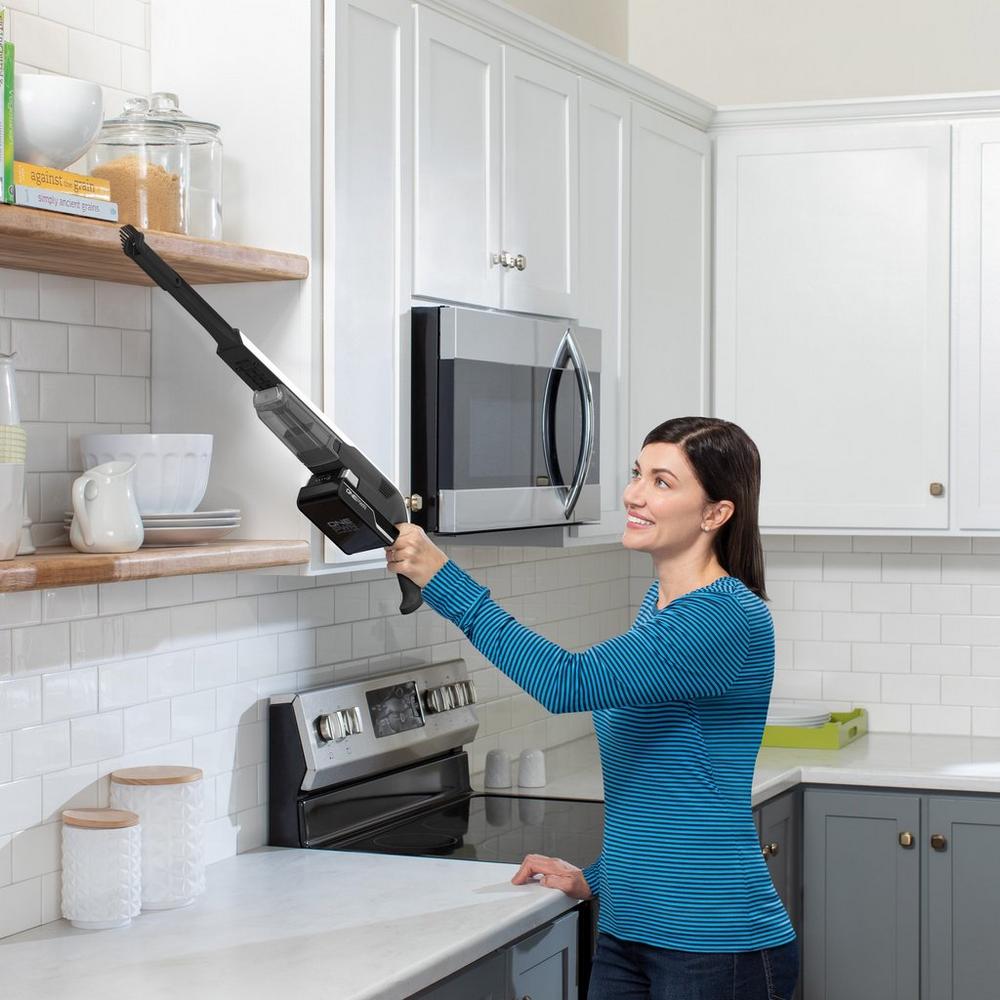 Person using a lightweight, cordless handheld vacuum to clean high shelves in a kitchen, demonstrating the vacuum's portability and ease of use for above-floor cleaning.