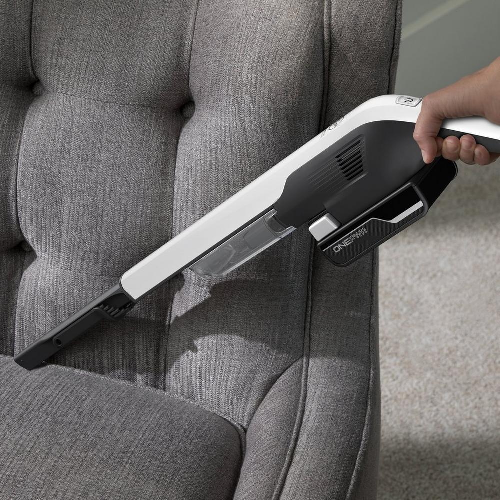 Handheld vacuum with a dusting crevice tool attachment, cleaning a gray upholstered chair, showcasing its versatility and effectiveness in reaching tight spaces.