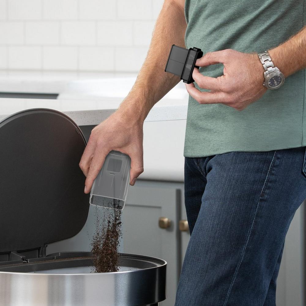 Person emptying the dirt cup from a handheld vacuum into a trash can, demonstrating the easy-to-empty feature of the devices.