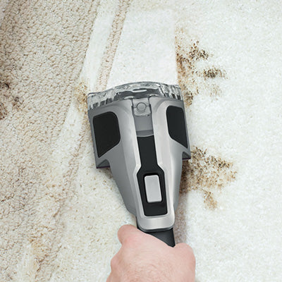 Close up of a hand using the pet tool to deep clean dark brown stains from a white carpet