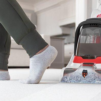 Close-up of a Hoover carpet cleaner in use, with a person's foot in socks nearby, highlighting the cleaner's effectiveness in revitalizing carpet cleanliness.