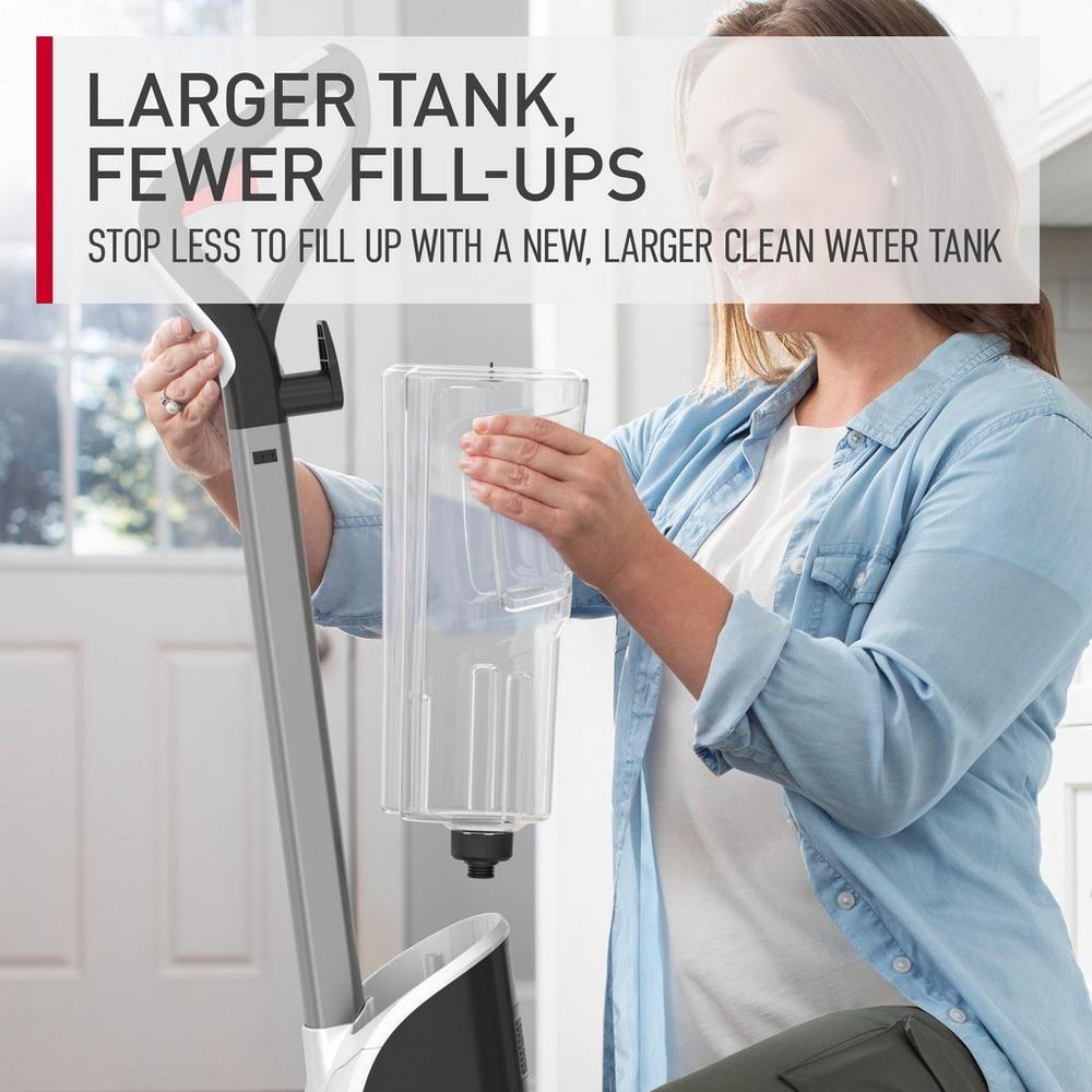 Woman demonstrating the larger clean water tank of a Hoover carpet cleaner, designed for fewer fill-ups during cleaning, showcasing its practical and user-friendly features.