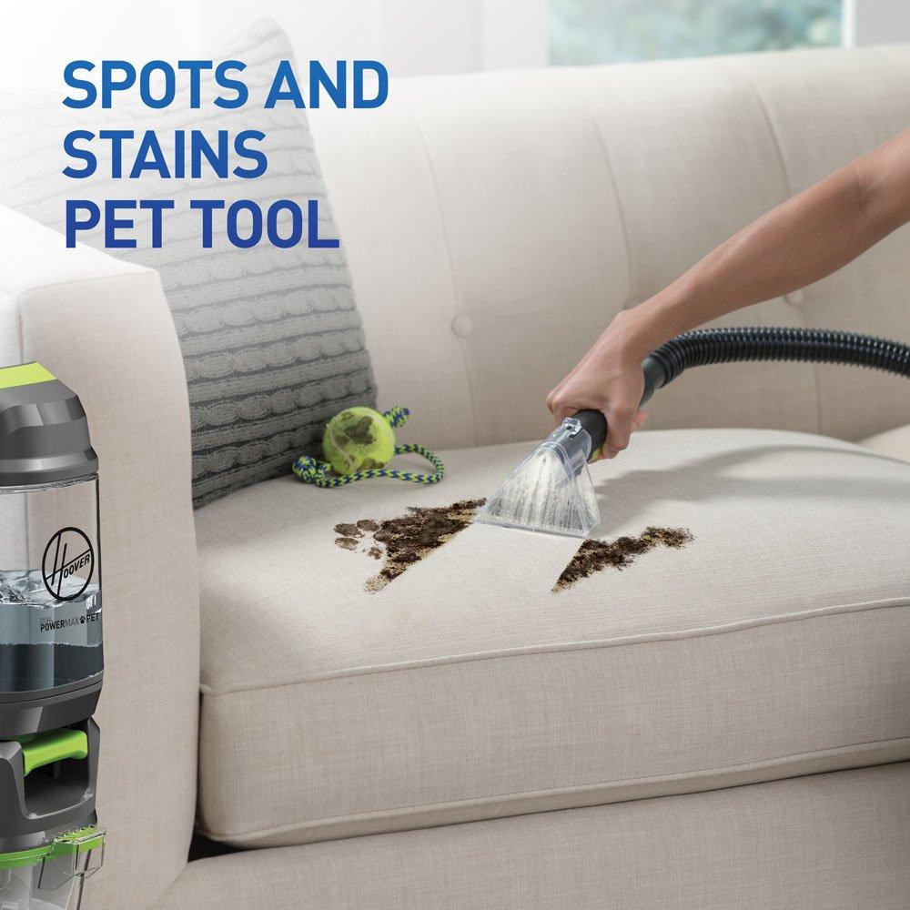 User demonstrating the Spots and Stains Pet Tool, effectively removing pet stains from a beige sofa, with a Hoover cleaner visible in the background.