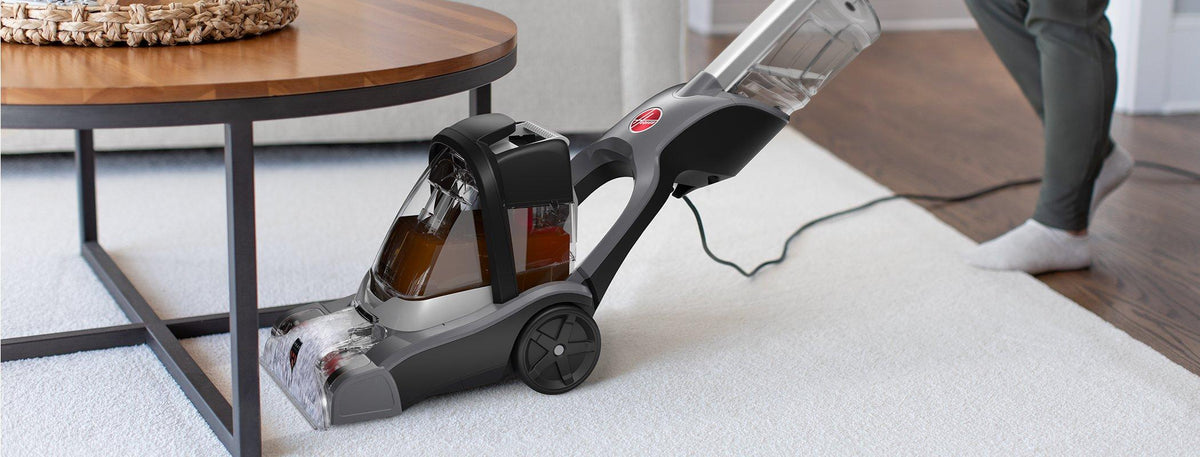 Hoover powerdash pet advanced carpet cleaner being used to clean under a low coffee table highlighting its flexibility to reach tight spaces
