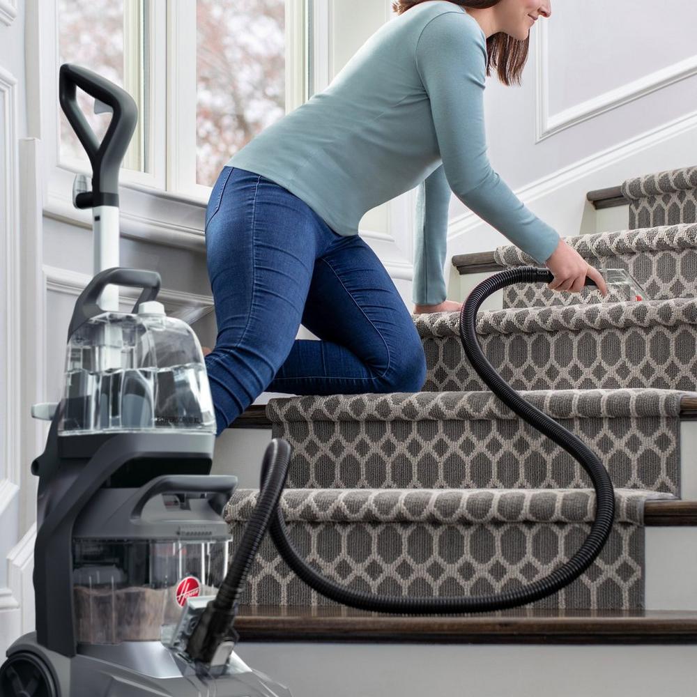 Woman using a Hoover carpet cleaner on stairs, showcasing the machine's hose attachment for effective cleaning of carpets in hard-to-reach areas.