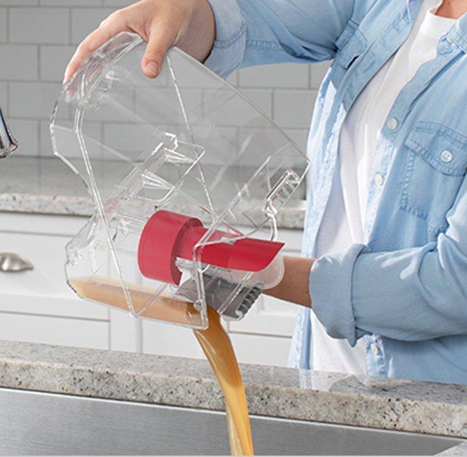 Person pouring out the contents of a transparent clean water tank from a Hoover carpet cleaner, showcasing its design for easy maintenance and cleanup.