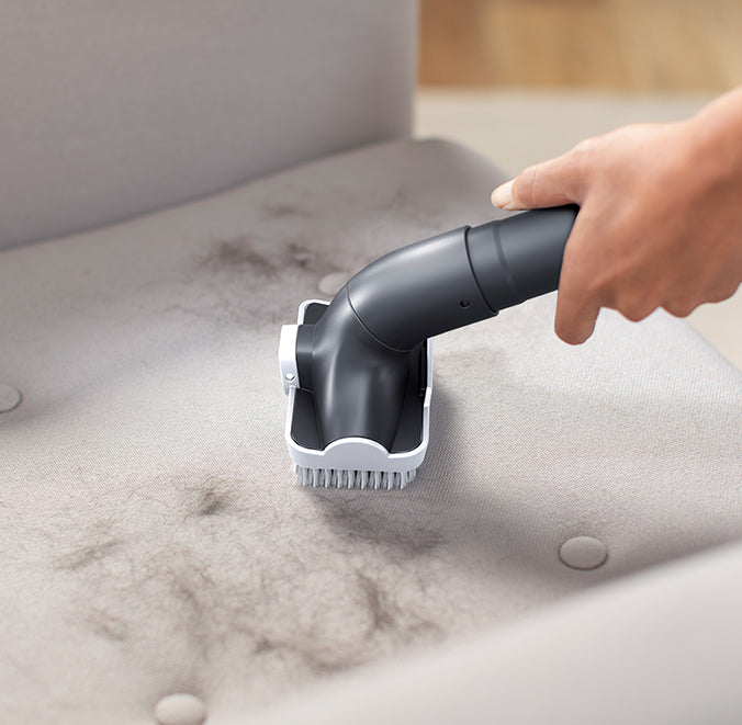 Close up of Hoover vacuum cleaner's 2 in 1 upholstery tool being used to clean pet hair from couch upholstery.