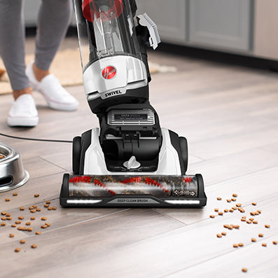 Hoover swivel vacuum cleaner effectively cleaning up scattered pet food on tiled kitchen floor.