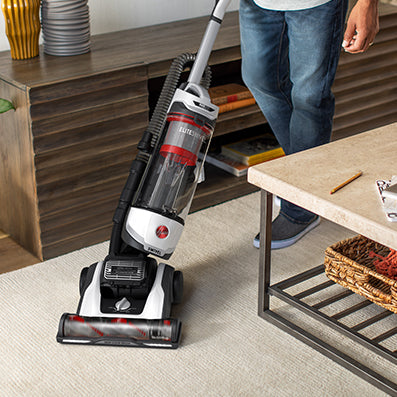 Hoover vacuum cleaner is shown maneuvering around a coffee table on a light colored carpet demonstrating its effortless swivel steering.