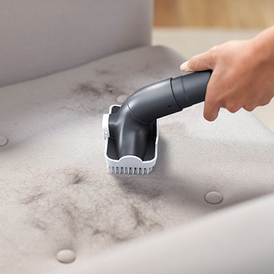 Close up of Hoover vacuum cleaner's 2 in 1 upholstery tool being used to clean pet hair from couch upholstery.