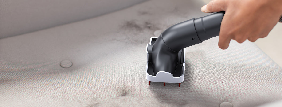 A hand using a specialized tool attachment to remove pet hair from a fabric surface, highlighting its effectiveness in cleaning pet hair