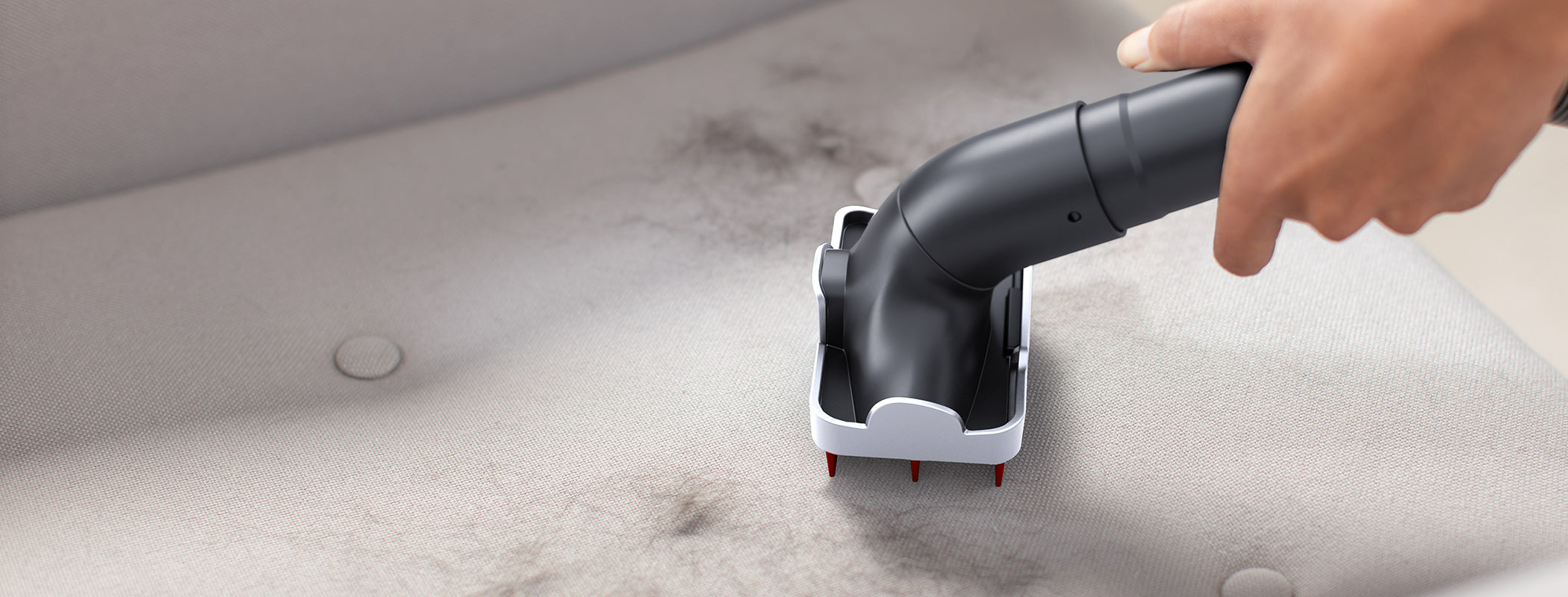 A hand using a specialized tool attachment to remove pet hair from a fabric surface, highlighting its effectiveness in cleaning pet hair