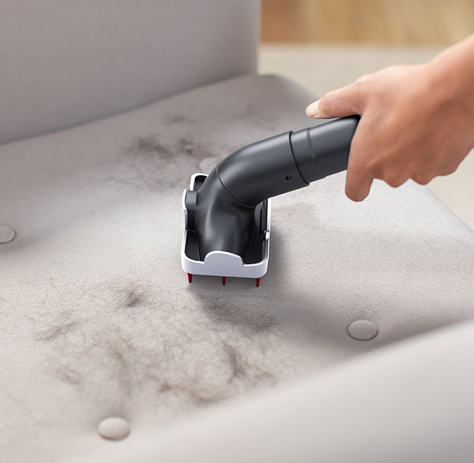 A hand using a specialized tool attachment to remove pet hair from a fabric surface. The image includes the text "say goodbye to pet hair with specialized pet tools," highlighting their effectiveness in cleaning pet hair