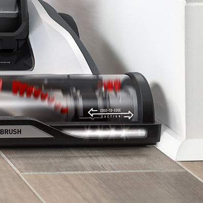 Close up of Hoover vacuum cleaner being used alongside the baseboards highlighting a more powerful motor and windtunnel technology that creates edge-to-edge suction.