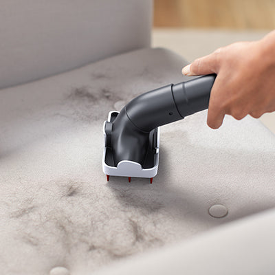 A hand using a specialized tool attachment to remove pet hair from a fabric surface, highlighting its effectiveness in cleaning pet hair