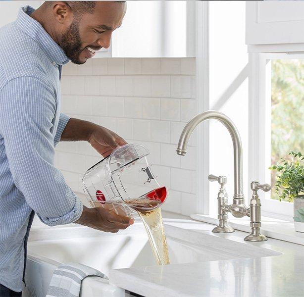 Man pouring dirty water from a Hoover carpet cleaner's tank into a sink, showcasing the dual tank system that separates clean and dirty water for effective cleaning.