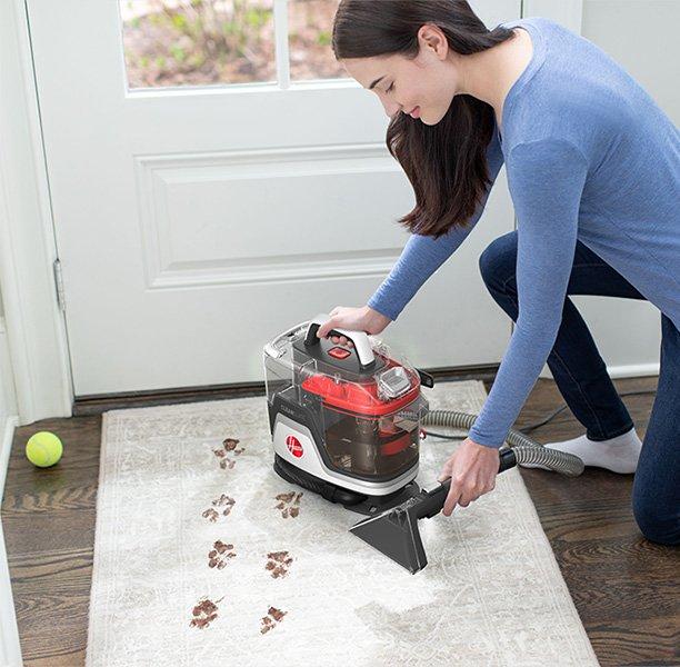 Woman using her Cleanslate portable spot cleaner to clean muddy paw prints out of a white area rug