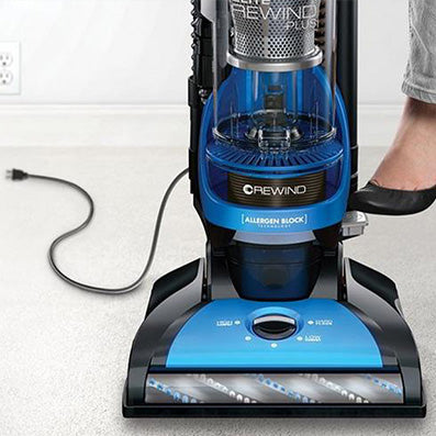Close up of a person using the foot pedal on a Hoover vacuum cleaner to activate the automatic cord rewind feature, highlighting convenience and ease of use.