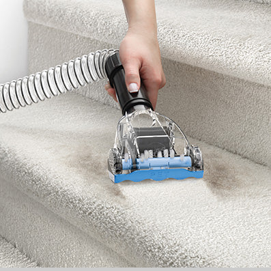 Hand using a hoover vacuum turbo tool on carpeted stairs