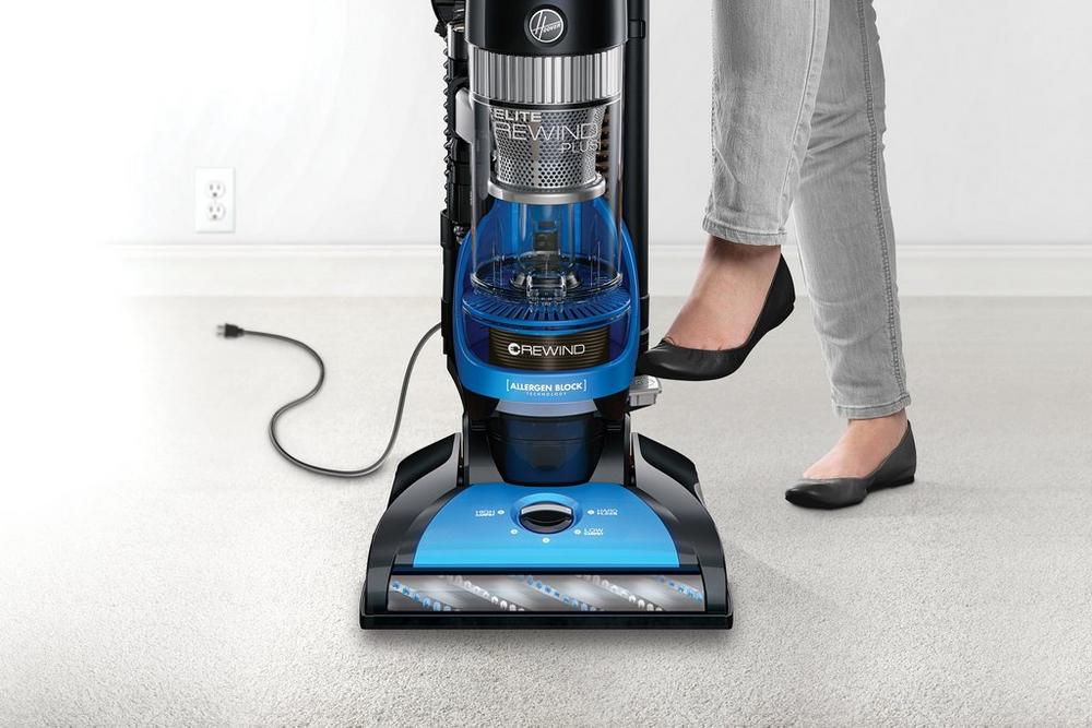Close up of a person using the foot pedal on a Hoover vacuum cleaner to activate the automatic cord rewind feature, highlighting convenience and ease of use.