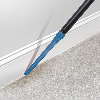 Using a Hoover crevice tool to clean along the baseboard and carpet edge, highlighting precise and thorough cleaning in tight spaces
