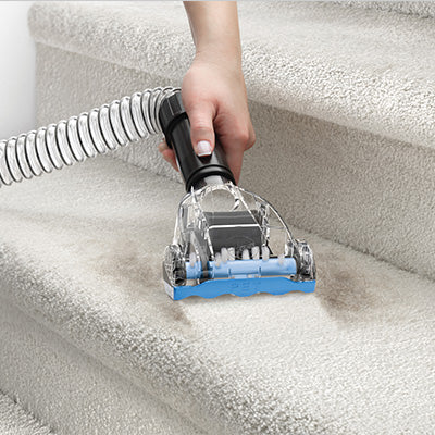 Hand using a hoover vacuum turbo tool on carpeted stairs