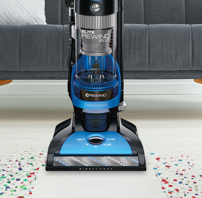Close up of Hoover vacuum cleaner in action on a white carpet with colorful confetti, highlighting its powerful suction and effective cleaning performance.
