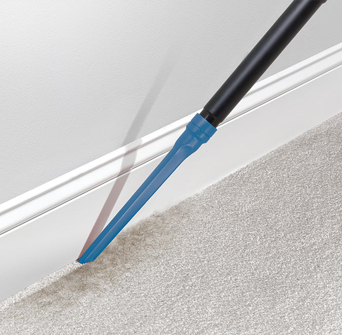 Using a Hoover crevice tool to clean along the baseboard and carpet edge, highlighting precise and thorough cleaning in tight spaces