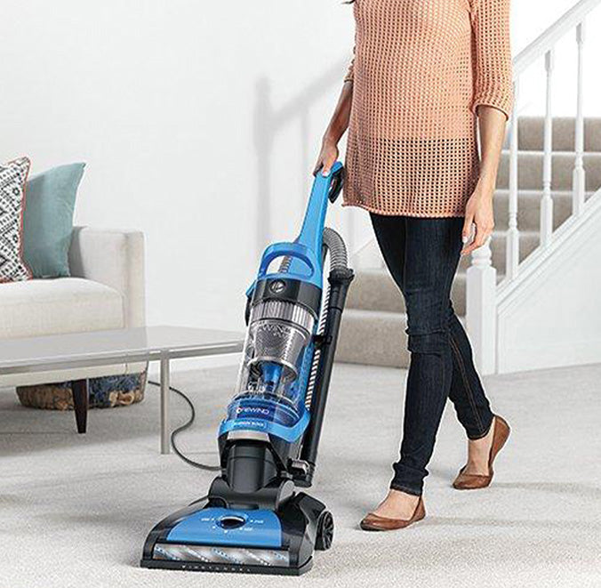 Woman vacuuming a white carpeted living room with a Hoover eilte rewind vacuum cleaner, showcasing it's effectiveness in maintaining clean and fresh carpets.