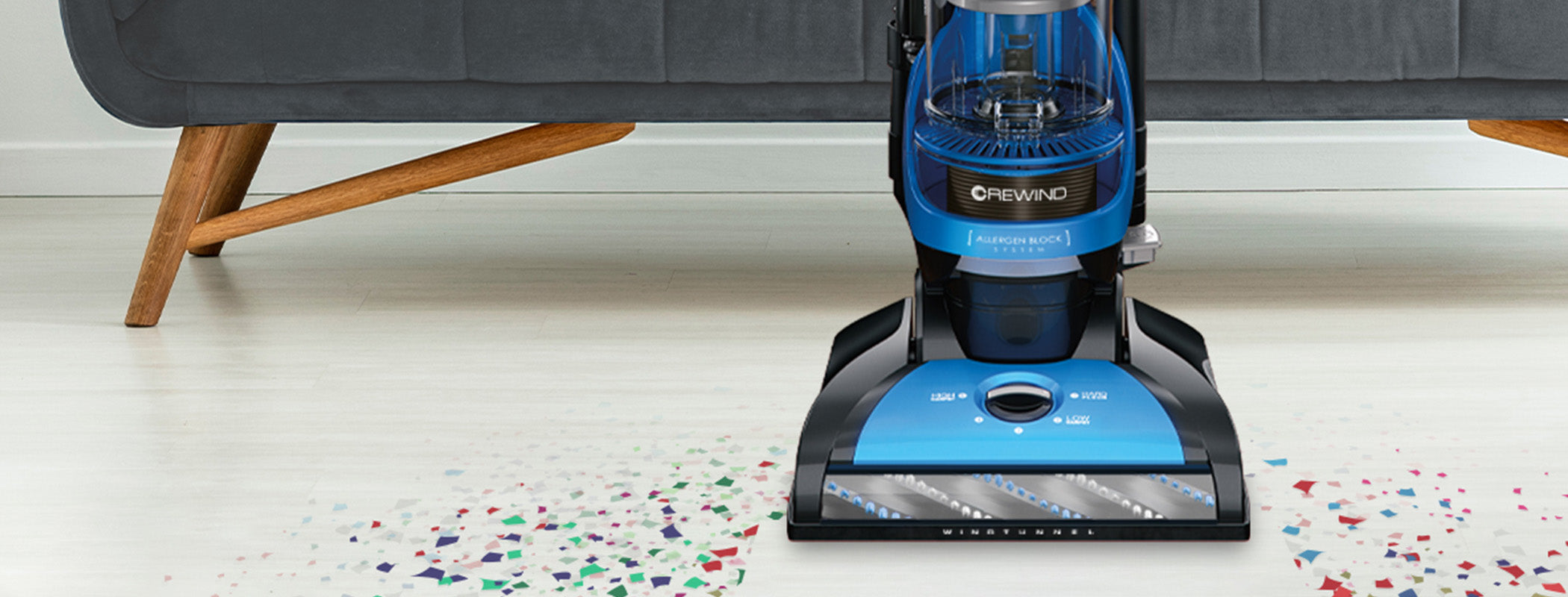 Close up of Hoover vacuum cleaner in action on a white carpet with colorful confetti, highlighting its powerful suction and effective cleaning performance.