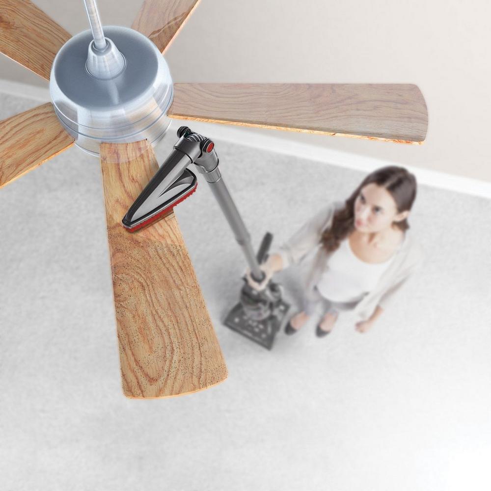 Woman using a Hoover pivoting dusting brush on a ceiling fan showcasing its ability to dust hard-to-reach areas like vents, ceiling fans, tops of bookshelves and more.