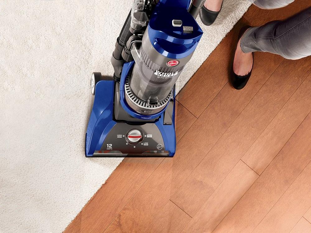 Close up of Hoover vacuum cleaner being used on a carpet and hard floor transition, showcasing its effective cleaning on multiple surfaces.