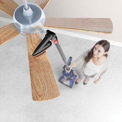 Woman using a Hoover pivoting dusting brush on a ceiling fan showcasing its ability to dust hard-to-reach areas like vents, ceiling fans, tops of bookshelves and more.