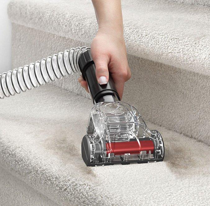 Close up of hand using the pet turbo tool to vacuum pet hair from stairs.